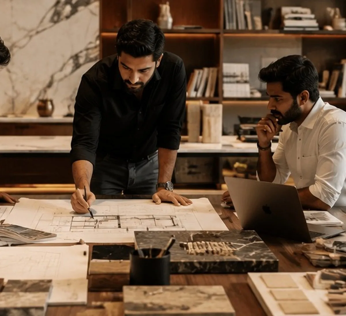 Two designers reviewing floor plans across a table spread with stone and timber samples
